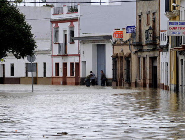 Una calle de Lora del R&iacute;o inundada; al fondo, tres vecinos cubiertos de agua hasta las rodillas.

Foto: Juan Carlos V&aacute;zquez