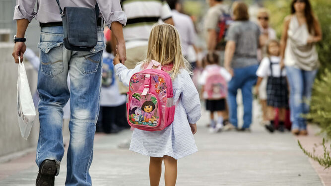 Una niña, de la mano de su padre, camino de su clase de preescolar.