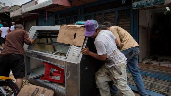 Tres venezolanos empujan una nevera ayer a las afueras de una carnicería que fue saqueada la noche anterior en Caracas.