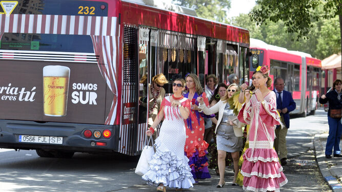 Varias mujeres vestidas de flamenca se bajan de un autobús de Tussam en la Portada.