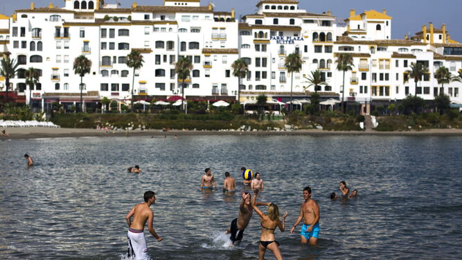 Varios bañistas, en primer plano, juegan con un balón, cerca de Puerto Banús.