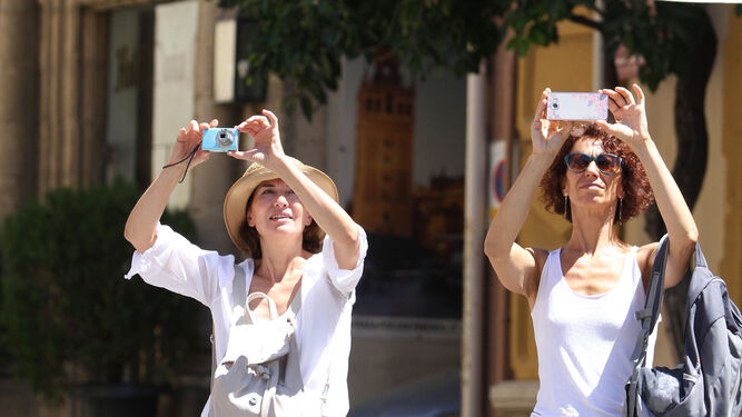 Dos turistas hacen fotos de la Giralda con sus móviles.