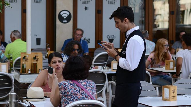 Un joven camarero sirve a dos clientas en una de las terrazas del centro de Málaga.
