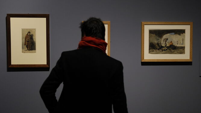 Uno de los visitantes de la exposición de Fortuny en El Prado observa tres cuadros.