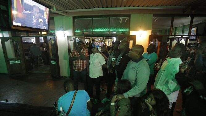 Varios ciudadanos siguen el discurso de Robert Mugabe a través de una televisión.