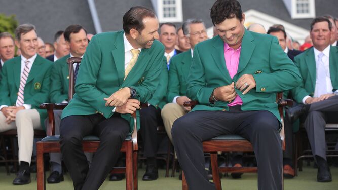 El ganador del Masters, Patrick Redd, intenta abrocharse la chaqueta verde junto al ganador en 2017, Sergio García.
