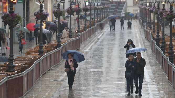Viandantes recorren la calle Larios bajo la lluvia esta Semana Santa 2024.