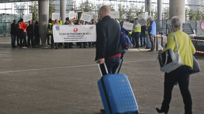 Dos turistas entran ayer en el aeropuerto con la concentración de los empresarios al fondo.