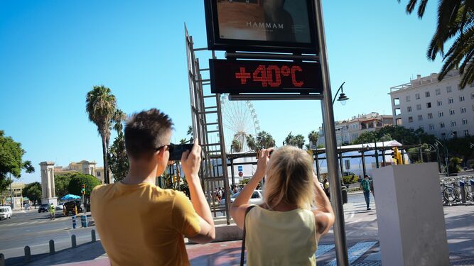 Dos turistas hacen fotos del termómetro  de la Plaza de la Marina.