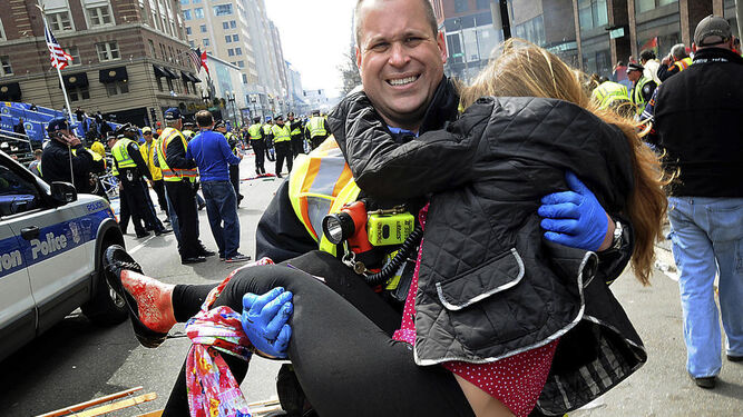 Un hombre traslada a una mujer tras el atentado del Maratón de Bostón.