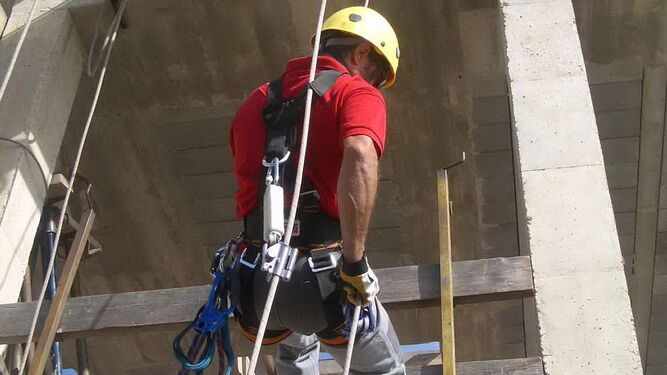 Un trabajador de una obra usando el arnés y sujeciones para prevenir riesgo de caídas.