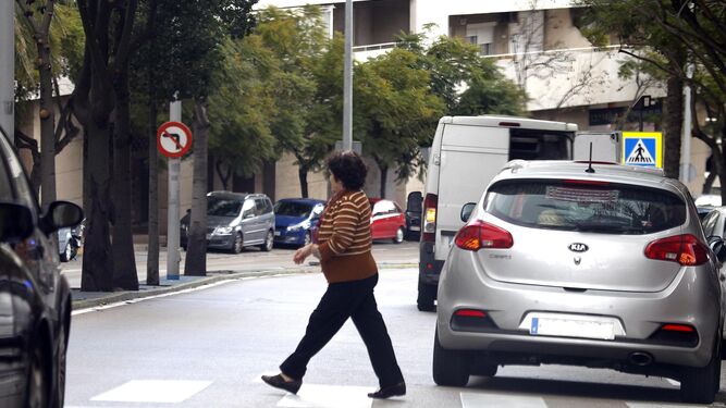 Una mujer pasa junto a un coche parad en doble fila.