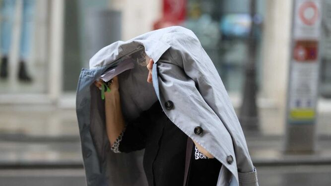 Una mujer se protege de la lluvia en Málaga con su abrigo.