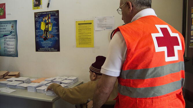 Un voluntario de Cruz Roja acompaña a votar a una persona con movilidad reducida.