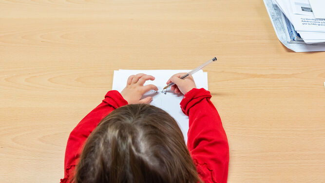 Una alumna dibujando en un folio sobre un pupitre.