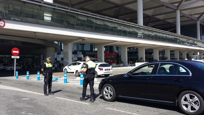 Dos policías locales observan un VTC parado en el aeropuerto de Málaga junto a una parada de taxis.