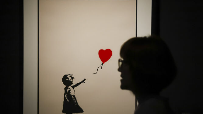 Una mujer pasa frente a la obra ‘Niña con globo’ de la exposición 'Banksy. The art of protest’.