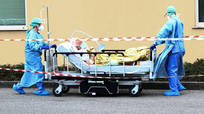 Dos trabajadores sanitarios trasladan a un afectado por coronavirus en el hospital italiano de Brescia.