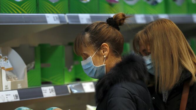 Dos mujeres con mascarilla y guantes se abastecen en un supermercado