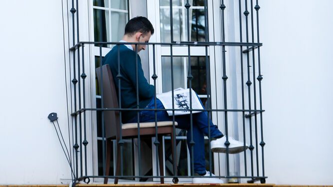 Un vecino confinado lee en el balcón de su casa.