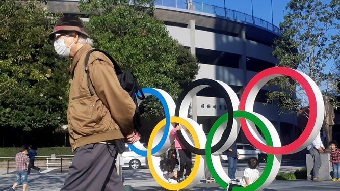 Un hombre protegido por una máscara pasa junto a los anillos olímpicos instalados en Tokio.