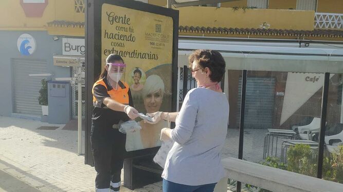 Una voluntaria de Protección Civil entrega una mascarilla a una mujer en una parada del autobús de Rincón de la Victoria.