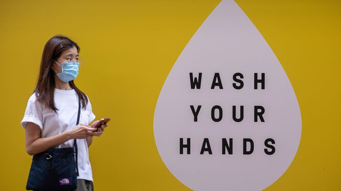 Una mujer china con mascarilla circula ante un cartel que invita a los ciudadanos a lavarse las manos contra el coronavirus.