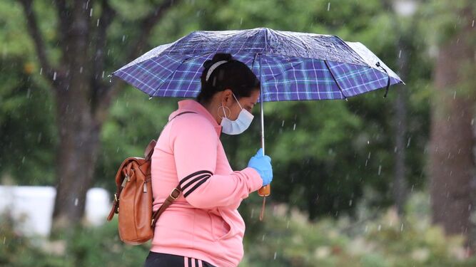 Una mujer, con mascarilla y guantes, se protege de la lluvia en Málaga capital.