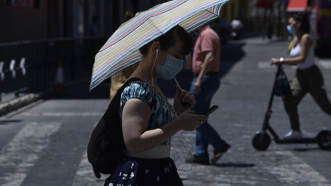 Una joven con mascarillas se protege del sol mientras maneja el móvil.