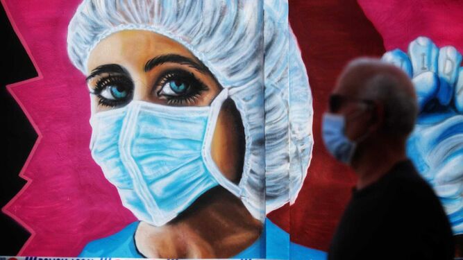 Un hombre con mascarilla pasa por delante de un mural dedicado a los sanitarios en Málaga.