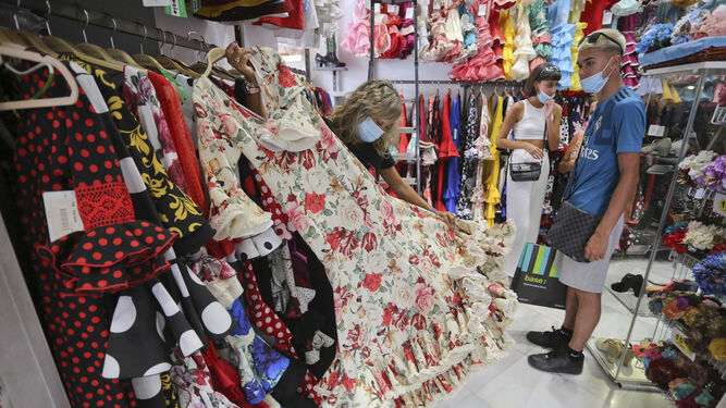 Una dependienta muestra un vestido de flores a unos clientes en El Rocío.