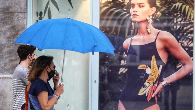 Dos personas, con paraguas y mascarilla, en el centro de Málaga.