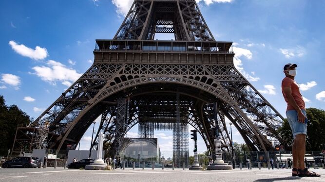 Un hombre con mascarilla pasa por delante de la Torre Eiffel.