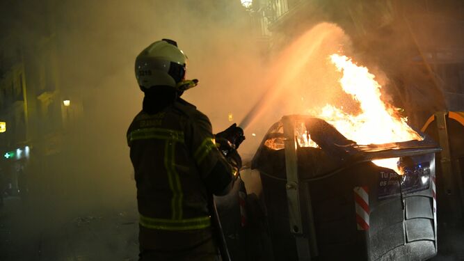 Un bombero extingue uno de los contenedores quemados