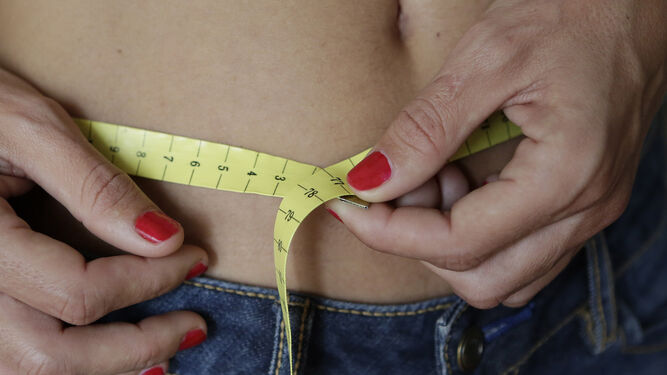 Una mujer se mide la cintura con un metro.