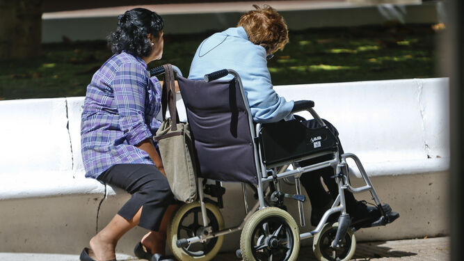 Una mujer en silla de ruedas junto a una cuidadora.