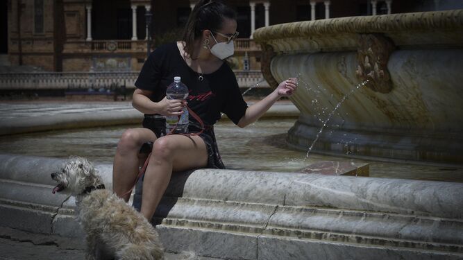 Una mujer con mascarilla se refresca en una fuente.