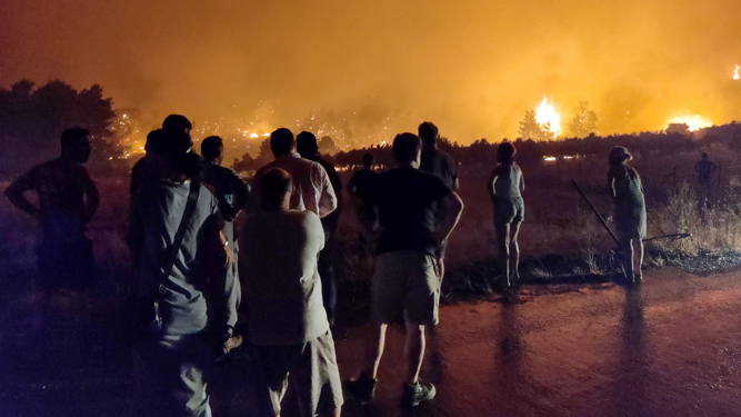 Varias personas contemplan uno de los incendios declarados en la isla griega de Evia.