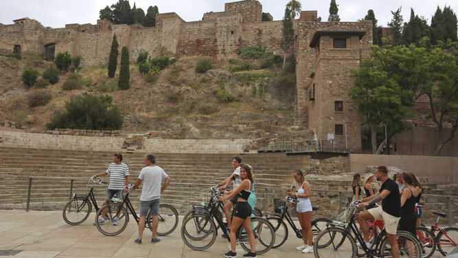 Un grupo de turistas en bicicleta en Málaga, frente al teatro romano y la Alcazaba.