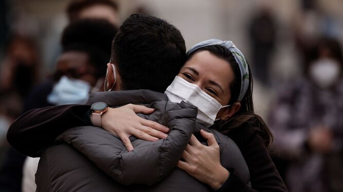 Dos jóvenes se abrazan en la calle con mascarillas.