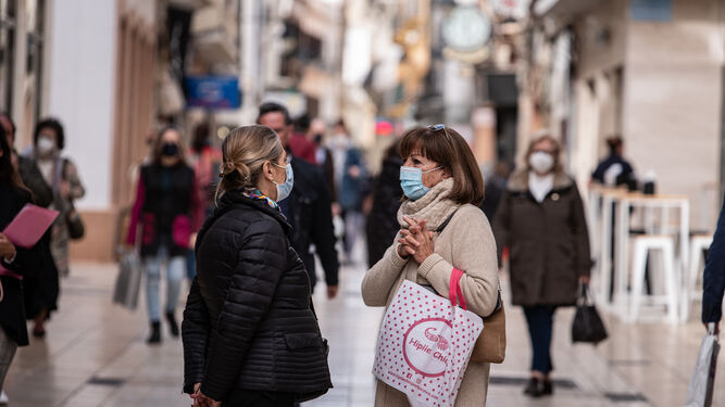 Dos mujeres con mascarillas conversan en una céntrica calle de Huelva