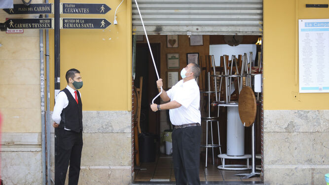 Dos trabajadores de un restaurante en Málaga abren la persiana.