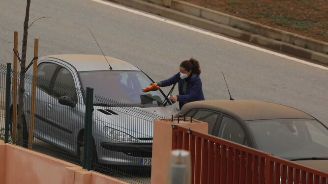 Una mujer, esta mañana, limpiando la luna delantera de su coche del barro en Málaga.