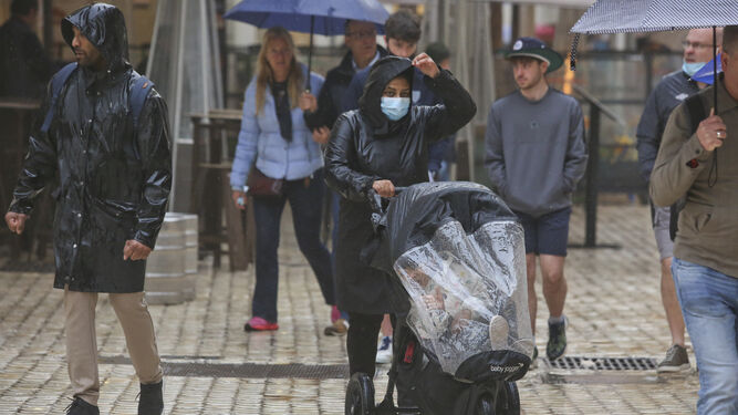 Varias personas se protegen de la lluvia en Málaga con chubasqueros y paraguas.