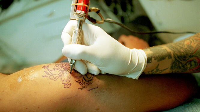 Un tatuador realiza un dibujo en el brazo de un joven.