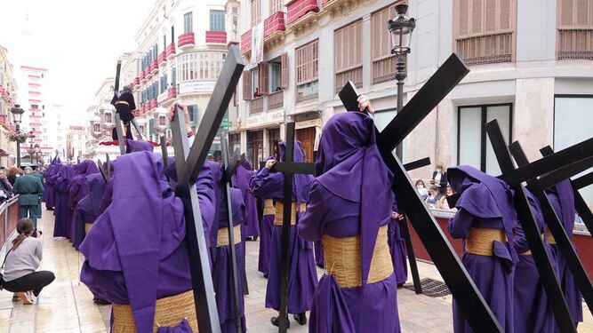 Nazarenos cargados con cruces siguen a Nuestro Padre Jesús de la Pasión en la calle Larios.