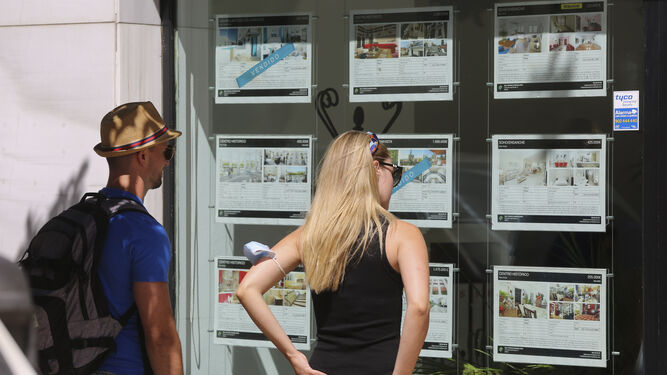 Dos jóvenes extranjeros miran el escaparate de una inmobiliaria en Málaga capital.