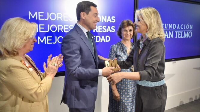 Juanma Moreno entrega el galardón a Claudia Hernández Rodríguez en presencia de Irene Navarro, presidenta de Ammde (a la derecha), y Rocío Medina, directora de la asociación en Andalucía Occidental