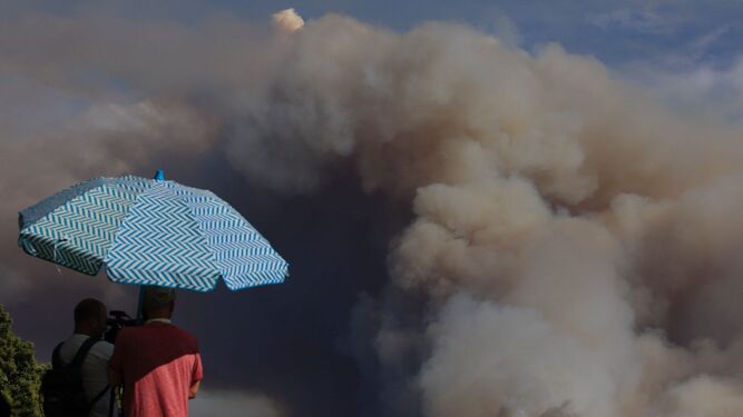 Fotógrafos se resguardan bajo un paraguas mientras toman imágenes del incendio.