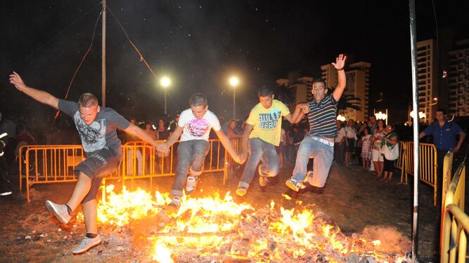 Varios jóvenes saltan juntos la hoguera de la playa en la Noche  de San  Juan